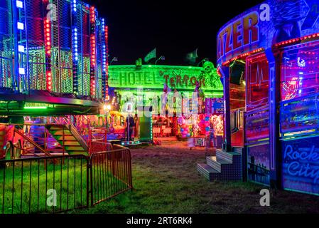 Un parco divertimenti notturno con una vivace giostra di carnevale illuminata da una ruota panoramica e da una giostra Foto Stock