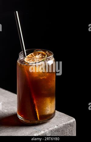 Cocktail alcolico rinfrescante in bicchiere con cubetti di ghiaccio e paglia guarnita con fetta di lime secca posta su un tavolo di pietra Foto Stock