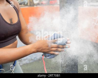 Dall'alto dell'anonima etnia femminile in abbigliamento sportivo mentre si stende e spolvera le mani sudorifere con il sacco in polvere di gesso alla luce del giorno contro le auto sfocate Foto Stock