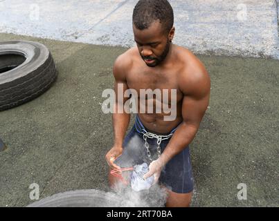 Dall'alto del maschio nero in abbigliamento sportivo sulle ginocchia e spolverare le mani del sudore con il sacco in polvere di gesso alla luce del giorno Foto Stock