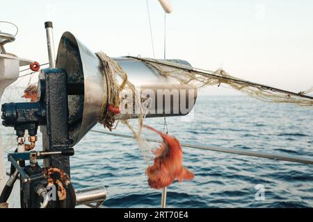 Barca da pesca con tamburo rotondo legato con rete da pesca e gamberi rossi appesi alla luce del giorno contro l'acqua marina blu sfocata e ondulata di Soller Mallorca in Spagna Foto Stock