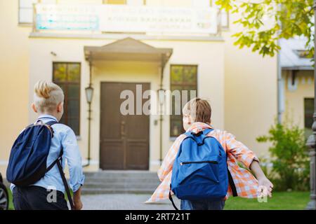 i bambini che corrono a scuola con gli zaini nelle giornate di sole. Inizio dell'anno accademico. Ragazzi vicino alla porta di scuola. Immagine con messa a fuoco selettiva Foto Stock