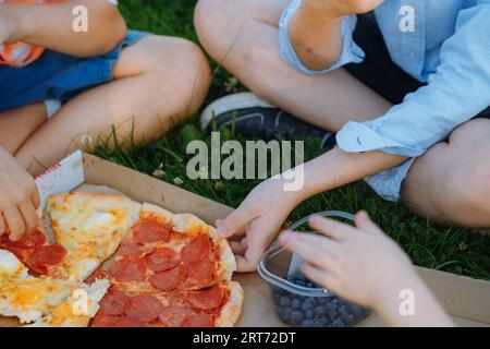 i bambini pranzano sull'erba dopo la scuola. I bambini afferrano fette di pizza. Immagine con messa a fuoco selettiva Foto Stock