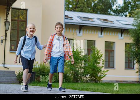 Felici bambini caucasici che scappano da scuola con zaini nelle giornate di sole. Inizio dell'anno accademico. Foto Stock