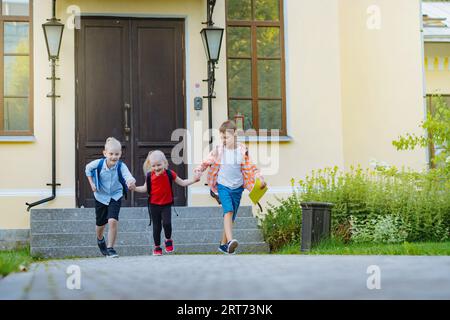 Felici bambini caucasici che scappano da scuola con zaini nelle giornate di sole. Inizio dell'anno accademico Foto Stock