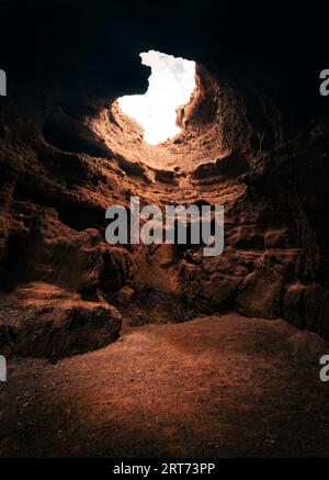 Una vista dell'interno della grotta con una splendida luce naturale dal cielo attraverso il buco. Grotta piena e scura vuota con luce soffusa. Foto Stock