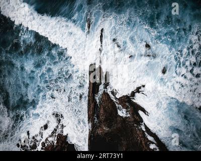 Foto aerea di un oceano forte e potente con onde enormi. Rocce e parte della scogliera all'interno dell'oceano blu tempestoso - vista dall'alto. Foto oscura e lunatica del dr Foto Stock