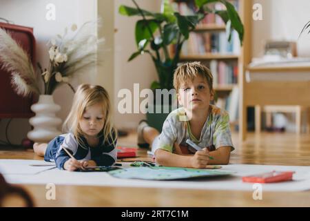 Fratelli sdraiati sullo stomaco e dipingono a casa con acquerelli, pennarelli e pitture a tempera, creando un modello del pianeta Terra. Foto Stock