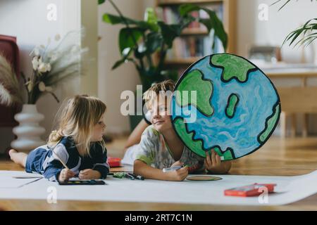 Fratelli sdraiati sullo stomaco e dipingono a casa con acquerelli e pitture a tempera, creando un modello del pianeta Terra. Foto Stock