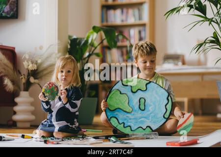 Fratelli che dipingono a casa con acquerelli e pitture a tempera, creando un modello del pianeta Terra. Foto Stock