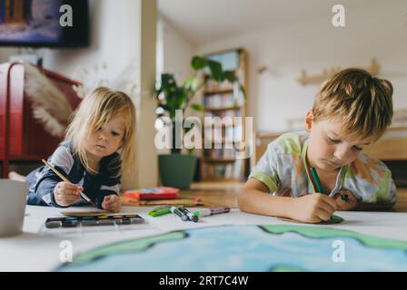 Fratelli sdraiati sullo stomaco e dipingono a casa con acquerelli, pennarelli e pitture a tempera, creando un modello del pianeta Terra. Foto Stock