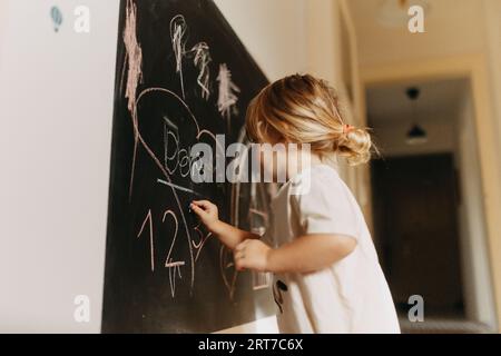 Una bambina che disegna su una lavagna con gesso. Foto Stock