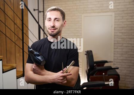 Il barbiere tiene in mano asciugacapelli, forbici e pettine Foto Stock