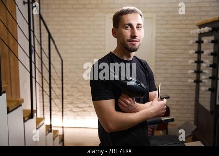 Il parrucchiere tiene tra le mani asciugacapelli, forbici e pettine Foto Stock