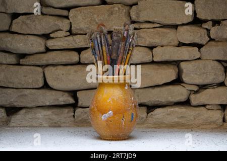 Un recipiente in ceramica arancione riempito con spazzole per vernice usate e sporche. Foto Stock