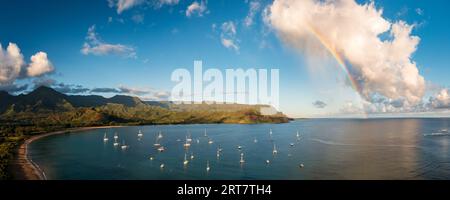 Vista aerea dell'arcobaleno e delle nuvole illuminate dal sole sulle cime delle montagne della costa di Na Pali attraverso la baia di Hanalei a Kauai Foto Stock