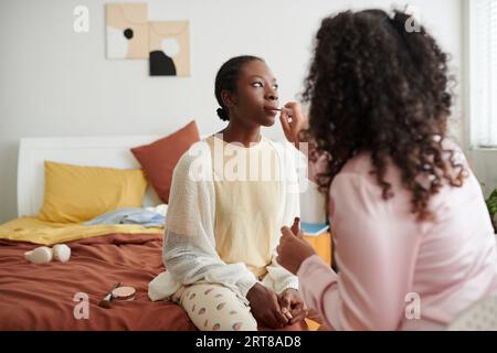 Ragazza che applica rossetto opaco quando si fa il trucco con gli amici Foto Stock