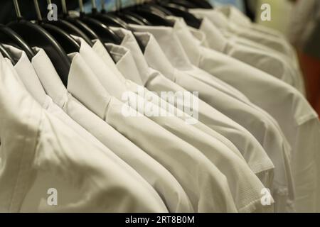 Le camicie bianche a maniche lunghe si appendono su appendiabiti in un negozio di abbigliamento. Primo piano. Foto Stock