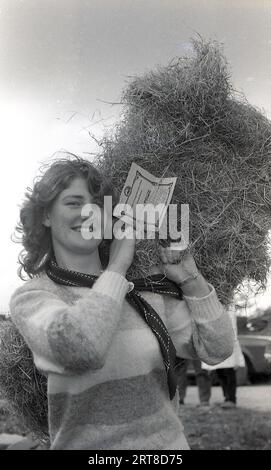 1983, storica, una giovane donna che regge una balla di paglia, ha vinto il secondo premio in un concorso di giovani agricoltori che si svolge al Silsden Young Farmers Club Annual Show nello Yorkshire, Inghilterra, Regno Unito. I club dei giovani agricoltori coinvolgono giovani di età compresa tra i 10-28 anni che amano l'agricoltura e la vita rurale. Foto Stock