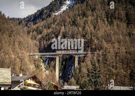 Zermatt, Switzerrland, 11 aprile 2017: Un treno rosso che attraversa un ponte ad arco a Zermatt Foto Stock