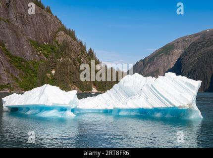 Iceberg che galleggia nel mare, sullo sfondo, la vista delle splendide montagne boscose. Foto Stock
