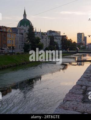 Edificio con cupola lungo il fiume Miljacka in una serata estiva nella città di Sarajevo, Bosnia ed Erzegovina, 11 settembre 2023 Foto Stock