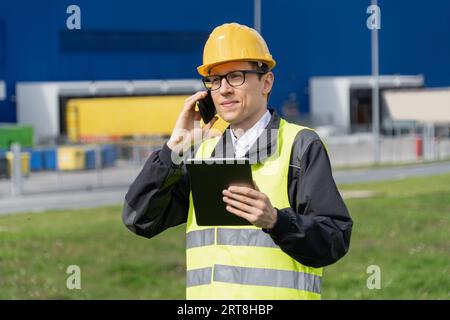 Logistician con telefono e tablet digitale su un background di centro logistico. Foto Stock