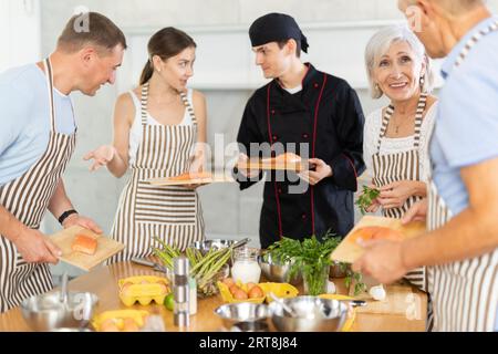 Lo chef in uniforme insegna agli studenti delle lezioni di cucina come pulire e tagliare il filetto di salmone Foto Stock