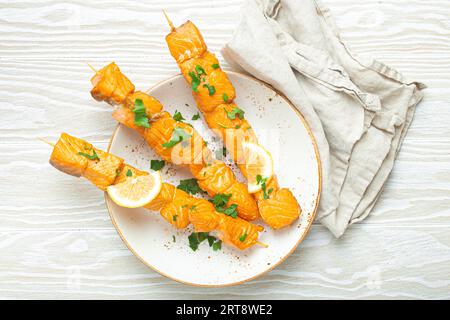 Spiedini di salmone alla griglia conditi con prezzemolo verde e limone su piatto di ceramica su tavola rustica in legno bianco vista dall'alto, salutare Foto Stock