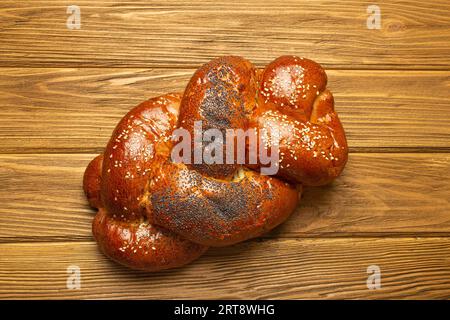 Pane Challah appena sfornato coperto di papavero e semi di sesamo, vista dall'alto su rustico sfondo di legno, tradizionale cucina ebraica festosa Foto Stock