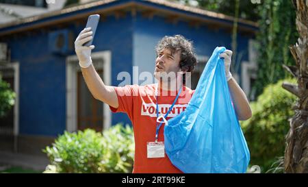 Un giovane attivista ispanico che tiene una borsa della spazzatura mentre effettua una videochiamata al parco Foto Stock