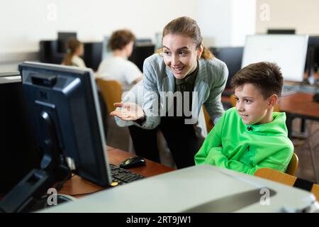 L'insegnante insieme agli studenti conduce una lezione sull'educazione informatica Foto Stock