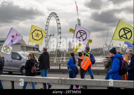 LONDRA - 24 aprile 2023: Unisciti ai manifestanti di crisi climatica che sventolano le bandiere XR sul Waterloo Bridge con l'iconico London Eye e le Houses of Parliament nel Foto Stock