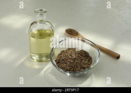 Semi di cumino persiano in ciotola e olio essenziale su tavola bianca Foto Stock