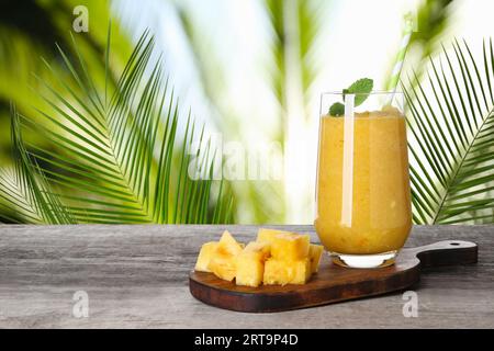 Gustoso frullato di ananas in vetro su tavolo in legno su sfondo sfocato, spazio per il testo Foto Stock