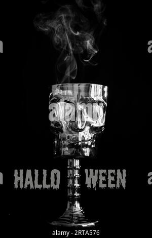 Cartello o invito per una festa di Halloween felice con una tazza decorativa a forma di teschio, fumando. Cartello di Halloween scritto in lettere grigie su sfondo nero. Copia Foto Stock