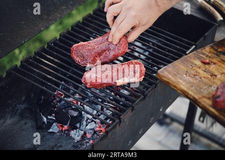 Un uomo irriconoscibile ha messo delle bistecche crude sulla griglia calda del grill Foto Stock