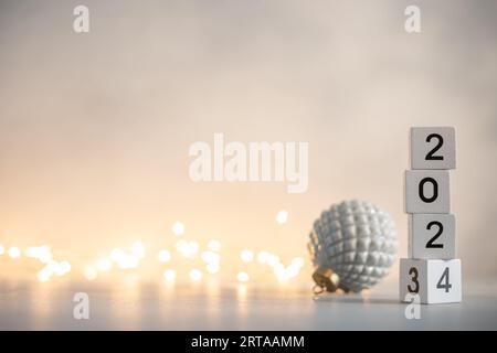 Capodanno 2024 in arrivo. Blocchi di legno bianco con data di Capodanno 2024 sul tavolo nella luce intima delle luci natalizie Foto Stock