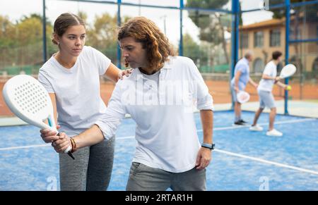 Giovane coach che insegna a un uomo di mezza età a giocare a padel sul campo da tennis all'aperto Foto Stock