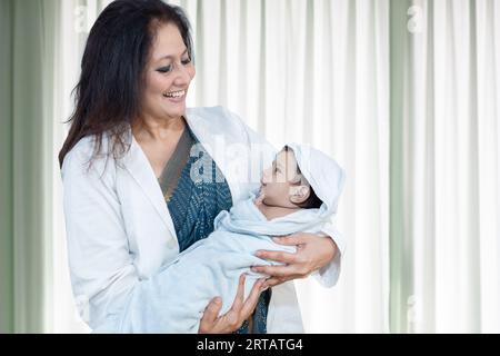 Giovane medico indiano o infermiera che tiene il neonato avvolto in una coperta. Ritratto di operatore medico con bambino neonato in reparto ospedaliero. Foto Stock