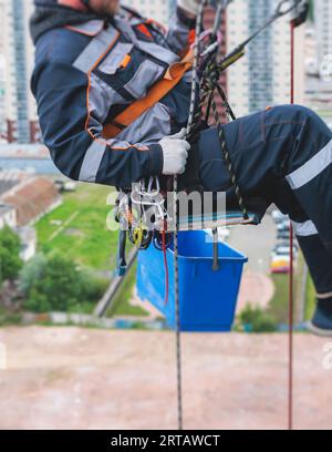 Operaio arrampicatore professionista che esegue lavori di pittura, riparazione e pulizia di finestre sulla facciata di un grattacielo residenziale, parete esterna di un alto grattacielo, Foto Stock