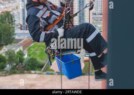 Operaio arrampicatore professionista che esegue lavori di pittura, riparazione e pulizia di finestre sulla facciata di un grattacielo residenziale, parete esterna di un alto grattacielo, Foto Stock