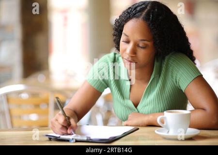 Donna nera che compila il modulo o il sondaggio seduto in una terrazza bar Foto Stock