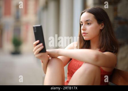 Donna seria che controlla i contenuti del telefono per strada Foto Stock