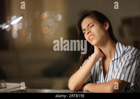 Donna stressata che soffre di mal di collo e si lamenta seduta la notte a casa Foto Stock