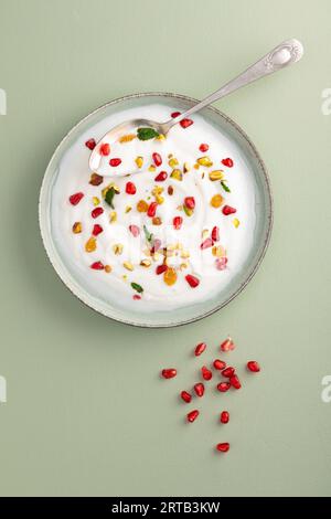 Yogurt con uva passa, pistacchi e semi di melograno in piatto su sfondo verde. vista dall'alto. Colazione sana, concetto di alimentazione sana Foto Stock