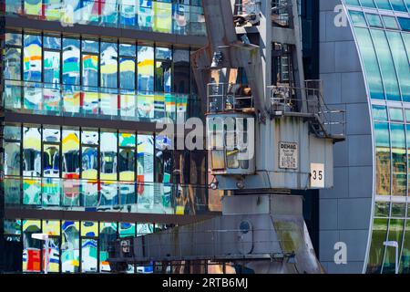 Vecchia gru di fronte alla facciata di vetro di un edificio di uffici, l'alto Colorium si riflette in essa, facciata con pannelli di vetro colorati, architetto W Foto Stock