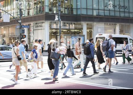 Turisti e newyorkesi attraversano la 5th Avenue lungo la 42nd Street in una calda giornata estiva nel centro di Manhattan. Foto Stock