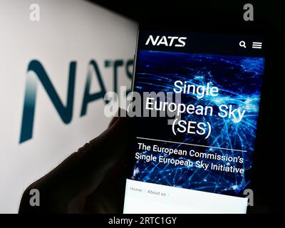 Persona che possiede uno smartphone con pagina web dell'operatore britannico di controllo del traffico aereo NATS Limited sullo schermo con logo. Concentrarsi sul centro del display del telefono. Foto Stock