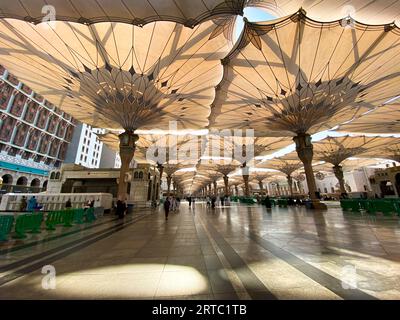 Medina, Arabia Saudita - 22 agosto 2023: I pellegrini camminano sotto ombrelli giganti nel complesso della Moschea Nabawi. Baldacchino a Masjid Nabawi a Medina, in Arabia Saudita Foto Stock
